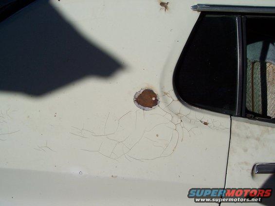 Close-up of a white car's side panel showing cracked paint and a rust spot near the rear window. A Supermotors.net watermark is visible