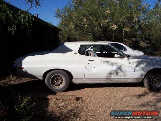 White 1972 Ford Ranchero coupe, side view, showing damage on the driver's door and a roll cage inside