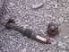 1995 Ford Bronco - A damaged driveshaft and differential flange lie on a bed of gravel, suggesting a significant mechanical failure.