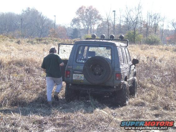 Rear view of a mud-covered SUV with a spare tire on the back, stuck in tall grass