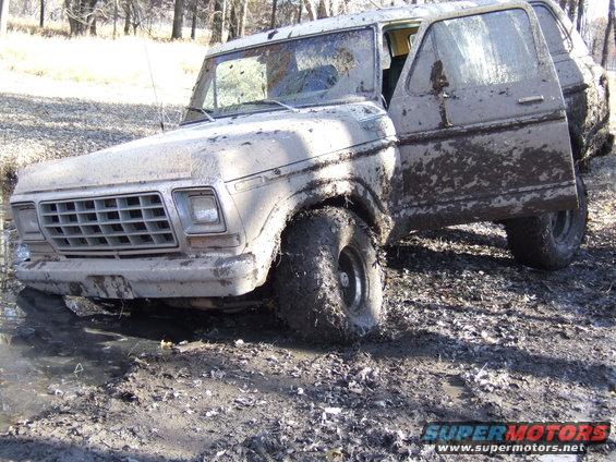 Muddy 1978 Ford Bronco with driver's door open, stuck in a muddy ditch