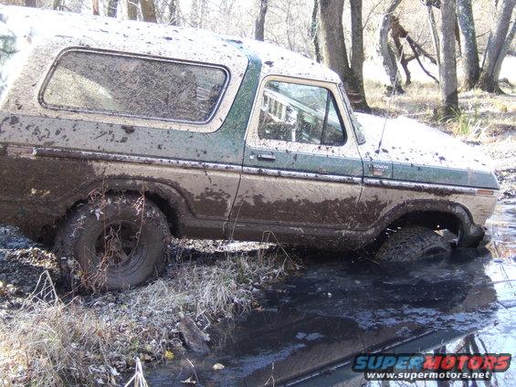 Mud-covered 1978 Ford Bronco stuck in water, side view