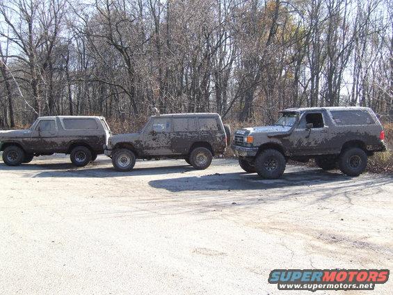 Three muddy SUVs parked on pavement with trees in background. The middle and right vehicles appear to be Ford Broncos from the 1980s