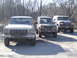 1979 Ford Bronco - Three off-road vehicles are parked in a lot with trees in the background.