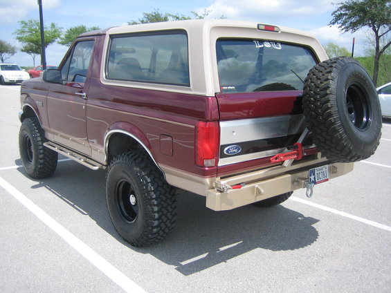 Maroon and tan Ford Bronco with lifted suspension and a spare tire on the back. Texas license plate visible