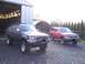 1990 Toyota 4Runner - Two Toyota 4Runners, a dark gray and a red model, are parked outside a garage.