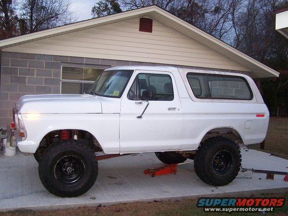 White SUV with lifted suspension, jacked up in front of a house