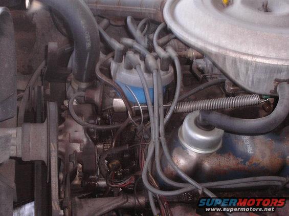 Close-up of an engine bay showing a blue-topped distributor, spark plug wires, and hoses