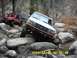 1996 Ford Bronco - Two off-road vehicles tackle a rocky trail in a wooded area.