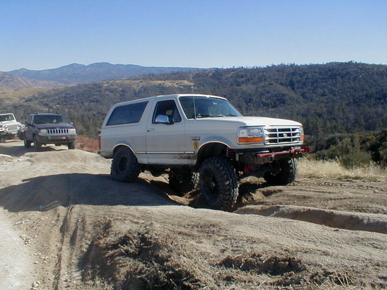 White 1996 Ford Bronco climbing a dirt hill with a Jeep and another SUV behind it
