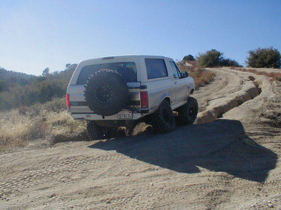 White 1992 Ford Bronco on a dirt trail, rear view, spare tire mounted externally