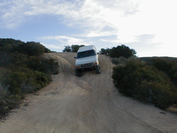 White SUV driving down a dirt hill off-road. It has a lifted suspension and off-road tires