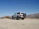 1996 Ford Bronco - A lifted Ford Bronco sits on a dusty trail under a clear blue sky, with mountains in the distance.