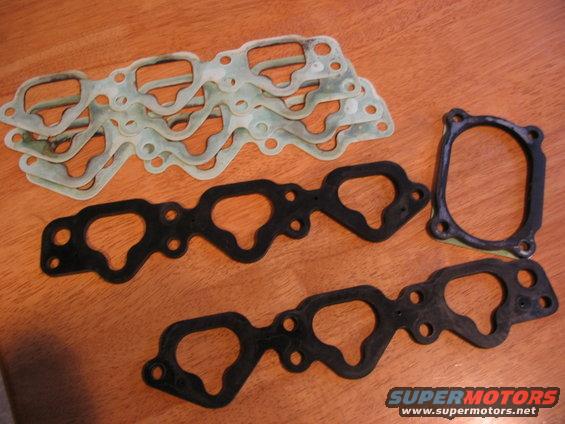 Engine gaskets on a wooden surface. Multiple light green and black gaskets are visible, some stacked