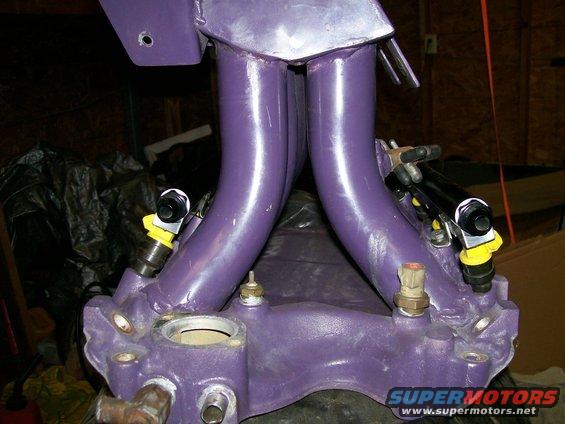 Purple intake manifold with fuel injectors attached. Some bolts and sensors are visible