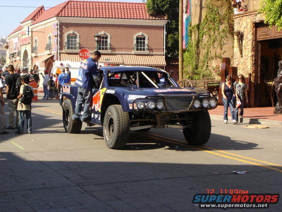 blue off-road race truck with red bull logos, front view, people around