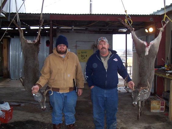 Two men stand with deer hanging from hooks