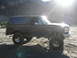 1993 Ford Bronco - Lifted dark brown 1993 Ford Bronco parked in a dusty, mountainous area with the sun flaring.