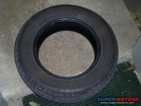 single tire is shown on a concrete surface with a green mat. Text on the tire is not legible