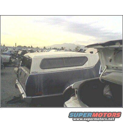 Pickup truck with camper shell in a junkyard, another car's trunk is open in foreground