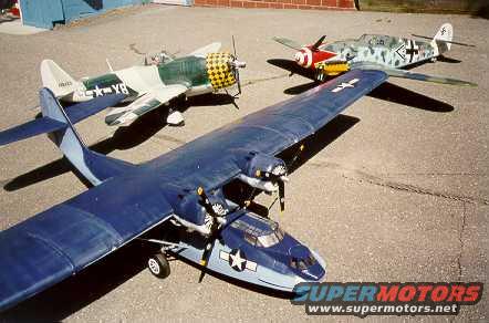 Model airplanes on pavement, including a large blue seaplane and two smaller fighter planes