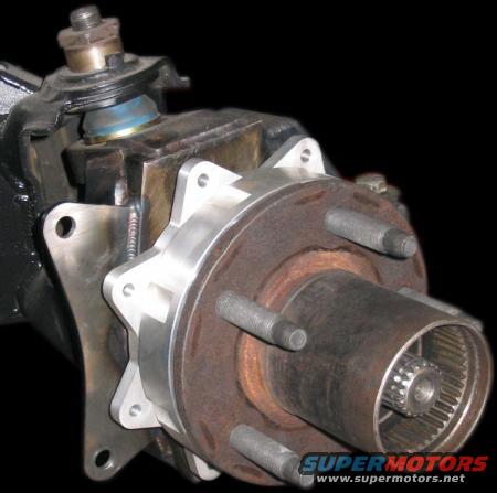 Close-up of a vehicle's front wheel hub assembly with a black background. Shows a rusty rotor, lug nuts, and splined axle shaft