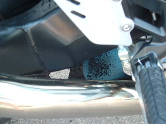 Motorcycle frame with welds, exhaust pipe, and footpeg. Blue sponge with black debris underneath