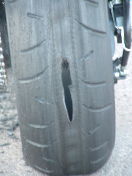 Close-up of a motorcycle tire showing a large, jagged gash in the tread