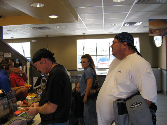 People at a counter in a fast food place, one guy in a white shirt, another in a black shirt, and a woman in denim