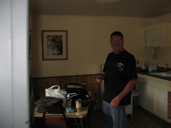 Man standing in a room with a table of bags and cans, and a kitchenette in the background