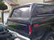 1978 Ford Bronco - Rear view of a dark blue 1978 Ford Bronco, showing its quarter panel and tailgate. Another vehicle is partially visible to the left.