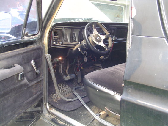 Interior of a dark-colored truck with a black seat, aftermarket steering wheel, and exposed wiring