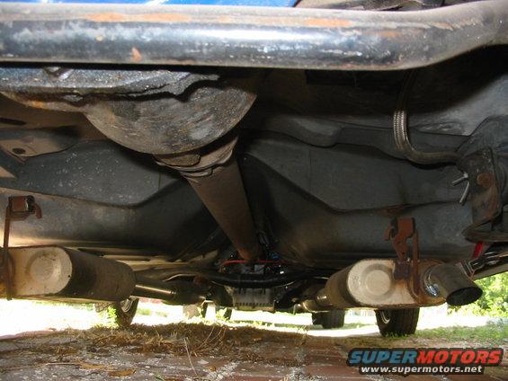 Undercarriage view of a car's exhaust system with dual mufflers and a driveshaft