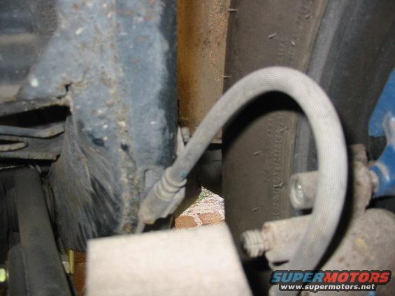 Close-up of a car's rear suspension components, including a brake line and part of the tire