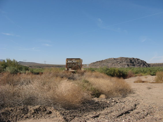 Metal structure in a dry, brushy landscape with a rocky hill in the background