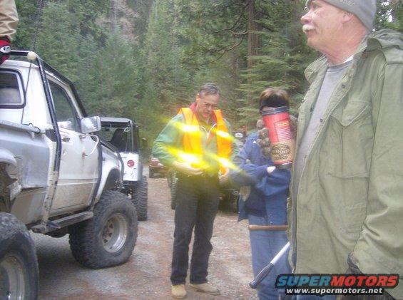 Several off-road vehicles parked in a wooded area with people around them