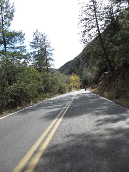 Motorcycle riding on a two-lane road through a wooded, hilly area