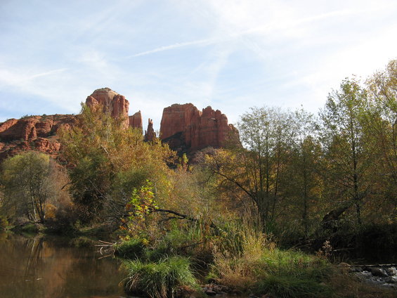 red rock formations rise above a river with trees in autumn colors