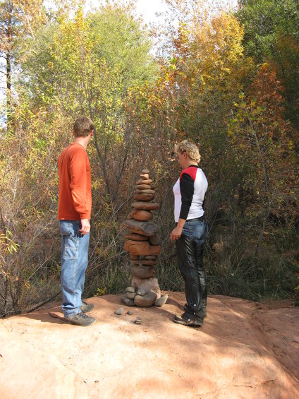 Rock cairn with two people observing it in a wooded area