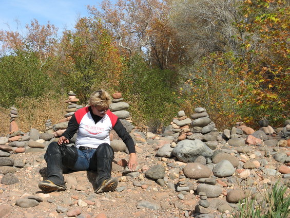 Woman in jeans and chaps sits on rocky ground, surrounded by numerous cairns