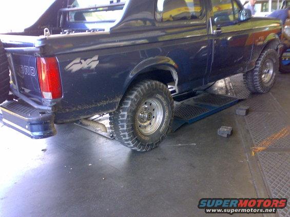 Dark blue Ford Bronco, rear view, on a lift. Has 4x4 decal on fender