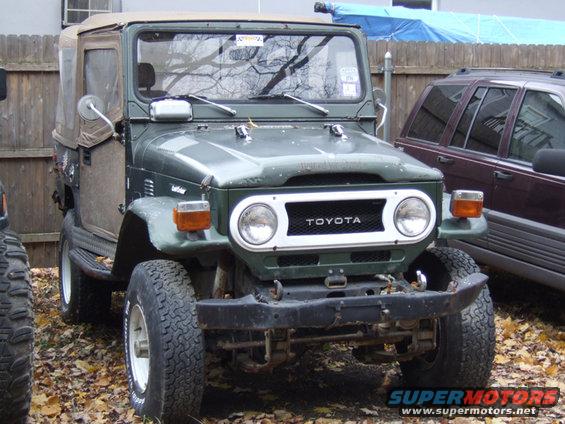 Green Toyota Land Cruiser with a tan soft top, parked next to another SUV