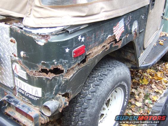 Heavily rusted rear quarter panel of a dark green SUV with a soft top and a 'TOYOTA Land Cruiser' badge