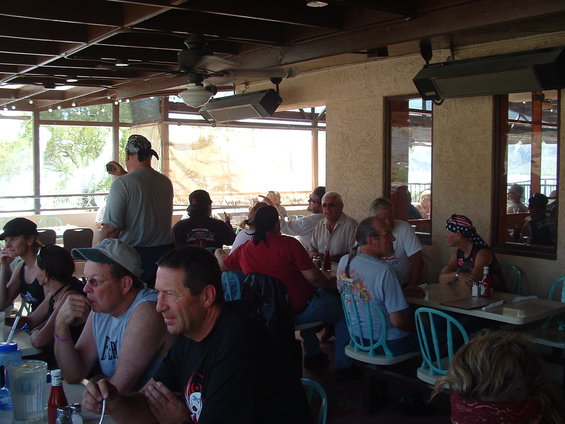Group of people sitting at tables on a patio, some wearing bandanas