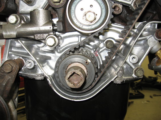 Close-up of engine timing belt, gears, and tensioner assembly. Part number '040' visible on housing