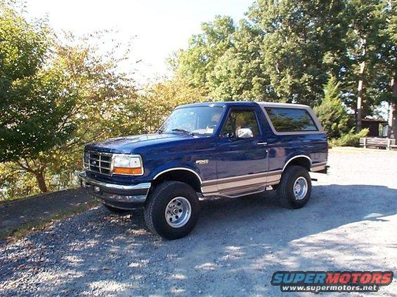 Blue Ford Bronco parked on a gravel lot with trees in the background