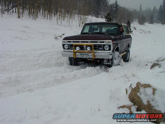 Maroon Ford Bronco driving in snow, front bull bar with lights, snow-covered tires