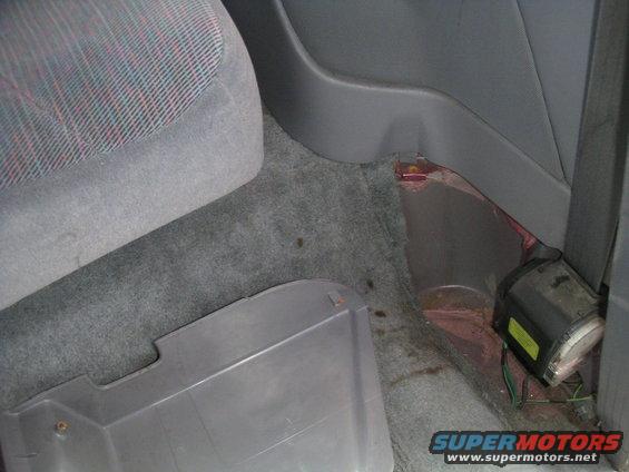 Vehicle interior showing gray carpet, seat fabric with red and blue threads, and a black seatbelt mechanism