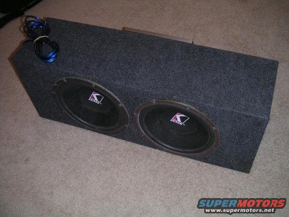 Dual Kicker subwoofers in a grey carpeted enclosure with blue speaker wire