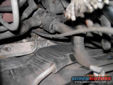 Close-up of engine bay hoses and metal components, with a watermark reading 'SUPERMOTORS.NET'